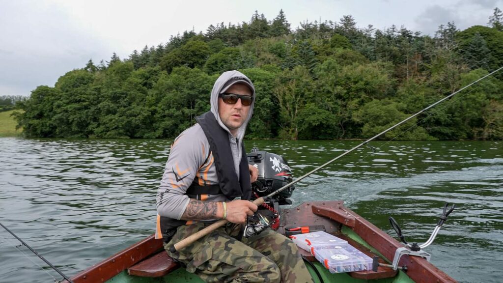 A skilled angler proudly holding a large pike, showcasing the successful catch with a backdrop of serene water and lush greenery.